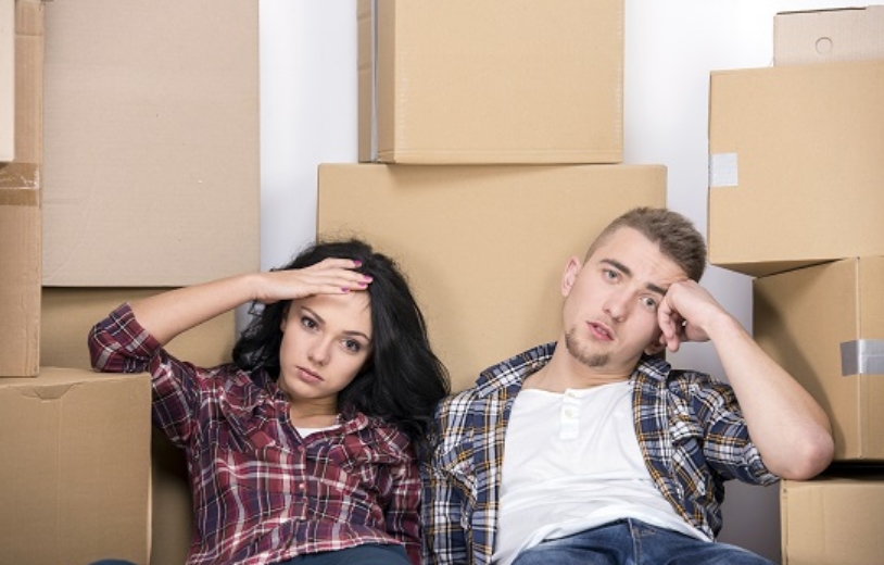 Couple looking exhausted in front of piles of moving boxes.